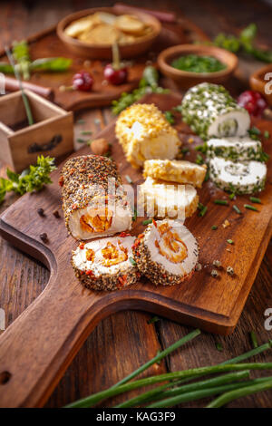 Soft cheeses rolled in herbs and spices on wooden cutting board Stock Photo