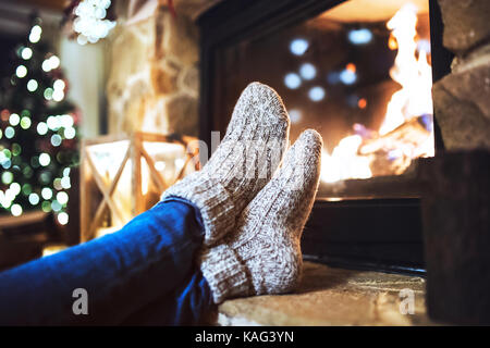 Feet of unrecognizable woman in front of the fireplace. Stock Photo