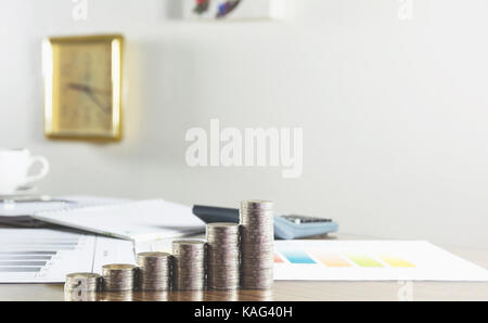 Closeup stack coin with documenton work table and the clock on white wall. Financial and saving concept. Stock Photo