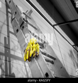 Yellow rubber gloves laid on the telescopic ladder next to the fresh painted wall of a wooden house, selective color square shot Stock Photo