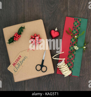 Christmas present gift wrapping background with parcel, tag, ribbon, scissors, coloured tissue paper, heart shaped bauble, holly, misteltoe and string Stock Photo