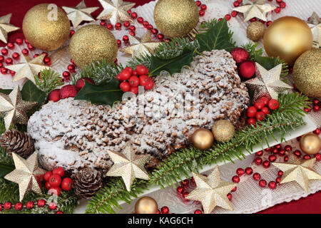 Chocolate stollen christmas cake on a plate with gold bauble and bead decorations, holly, fir and ivy. Stock Photo