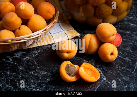 Ripe organic apricots harvested at summer time and big glass jar with canned sweet apricot compote on dark marble. Composition in rustic style - organ Stock Photo