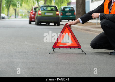 Close-up Of A Man Placing Warning Triangle With A Broken Down Cars Stock Photo
