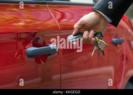 Close-up Of A Person's Hand Holding A Car's Remote Control Pointing To The Door Stock Photo