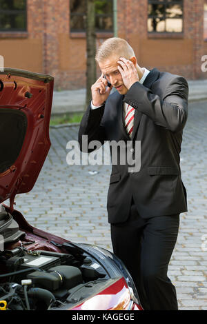 Stressed Young Man Calling On Cellphone For Service With His Breakdown Car Stock Photo