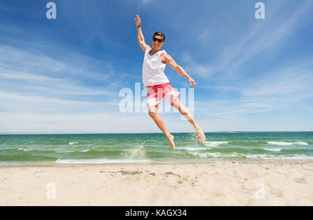 smiling young man jumping on summer beach Stock Photo