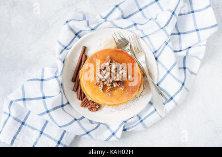 Stack of pancakes with pecan nuts, cinnamon and honey on white plate. Top view horizontal Stock Photo
