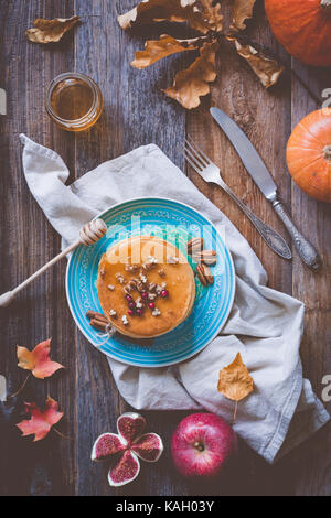 Pumkin pancakes on a blue plate on wooden background served with pecan nuts and honey. Autumn food still life Stock Photo