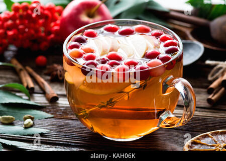 Herbal tea with cranberries, apple, giner, lemon, cinnamon and thyme in a glass. Warming tea, healthy fruit infused tea Stock Photo