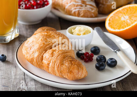 Continental breakfast fresh croissants with butter, glass of orange juice, jam and fruits on wooden table. Closeup view, horizontal Stock Photo