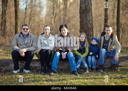Big happy family portrait sitting on a big log in early spring park Stock Photo