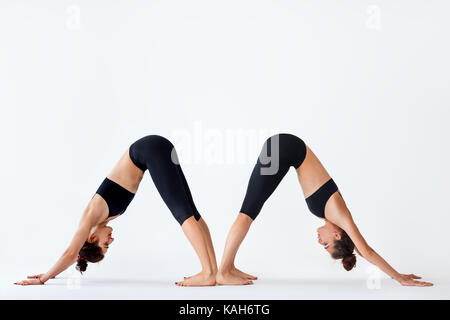 Two young women doing yoga asana Downward Facing Dog. Adho Mukha Shvanasana Stock Photo