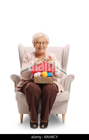 Mature woman seated in an armchair knitting and looking at the camera isolated on white background Stock Photo