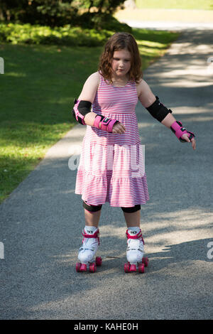 Young girl outside learning to riding on roller skates on driveway wearing protective elbow, wrist and knee pads Stock Photo