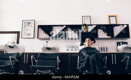 Woman sitting on salon chair while a hair stylist washing her hair. Hairdresser wiping the hair dry using a towel in the wash tub. Stock Photo