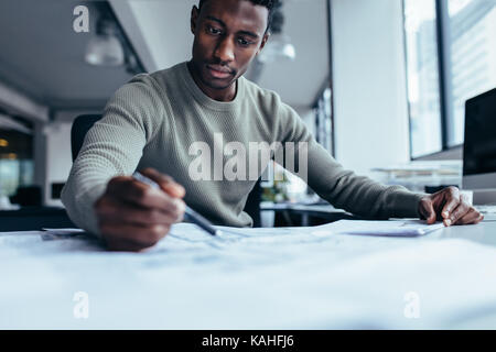 Businessman pointing at building plan in office. Black man working on construction plan. Stock Photo