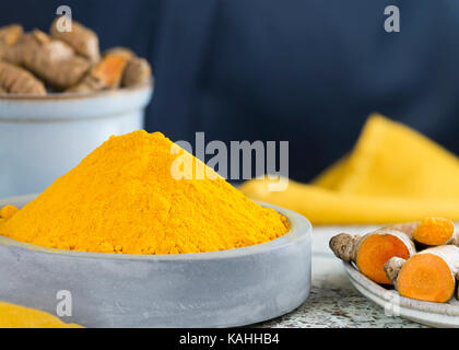 selective focus shot of powdered turmeric in a pile place in a light blue ceramic dish with raw root  a dark background copy space at header and side Stock Photo