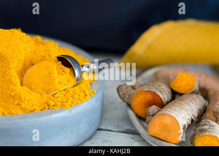 macro of turmeric spice in a blue clay bowl with with the raw roots to the side on a dark background copy space at the head of image Stock Photo