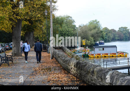 A couple walk along a leaf covered footpath alongside The River Thames at Windsor, UK. Stock Photo