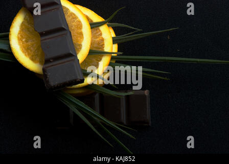 Fresh orange slices with green leaves and chocolate in a dark background Stock Photo