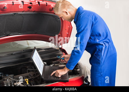 Mechanic Using Laptop While Repairing Car In Garage Stock Photo