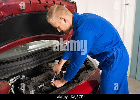 Young Mechanic Repairing Car Using Screwdriver In Garage Stock Photo