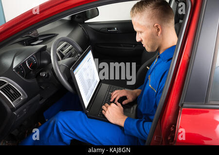 Young Mechanic Sitting In Car And Using Laptop Stock Photo