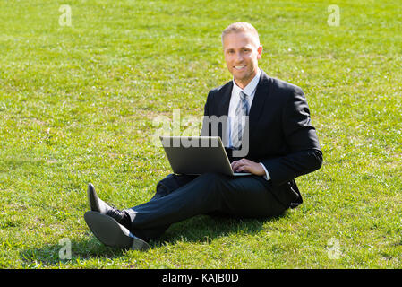 Businessman Sitting On Green Grass Using Laptop Stock Photo