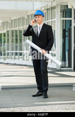Young Engineer Holding Blue Print Talking On Cellphone Stock Photo