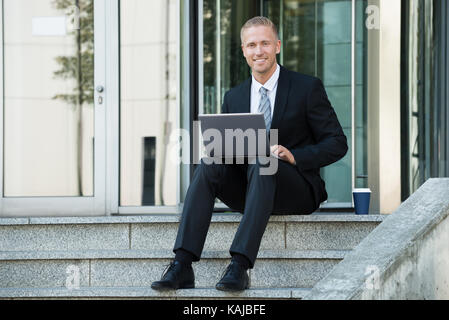 Happy Businessman Sitting On Stairs Using Laptop Stock Photo