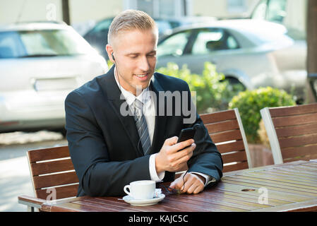 Businessman Sitting On Bench Listening Music On Cellphone Stock Photo