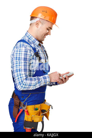 Side view portrait of young male construction worker with smartphone wearing protective clothes, helmet and tool belt isolated on white background Stock Photo