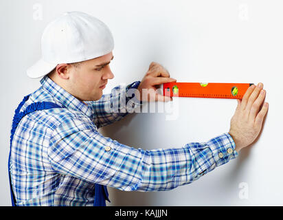 Young construction worker using spirit level on white wall Stock Photo