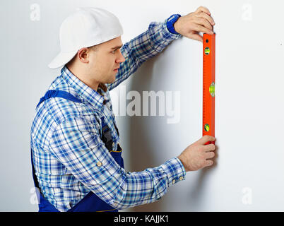 Young construction worker using spirit level on white wall Stock Photo