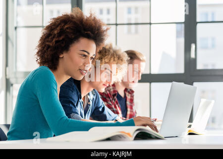 Side view of a happy student smiling while using a laptop for online information or virtual communication through social media during class at the uni Stock Photo