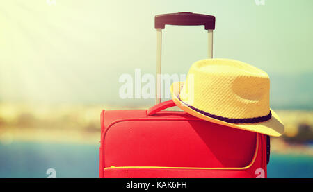 Hat and red suitcase closeup. Summer vacation and travel concept. Suitcase and yellow hat on soft sea background. Stock Photo