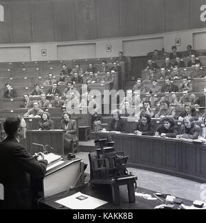 1950s, smartly dressed university students attending a class given by a male professor at the lecturn in the main chemistry lecture theatre at Leeds University, Leeds, England, UK. Stock Photo