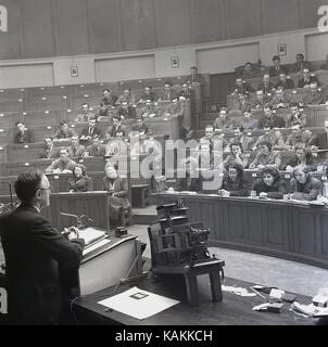 1950s, smartly dressed university students attending a class given by a male professor at the lecturn in the main chemistry lecture theatre at Leeds University, Leeds, England, UK. Stock Photo