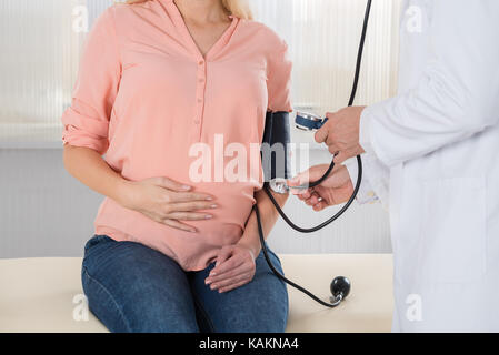 Midsection of male doctor checking pregnant woman's blood pressure in hospital Stock Photo