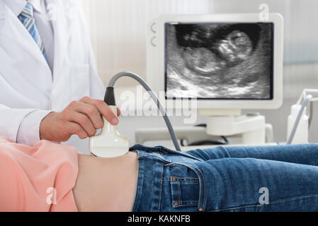 Cropped image of male doctor moving ultrasound probe on pregnant woman's belly Stock Photo