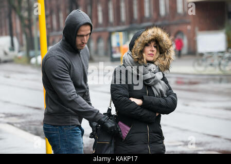 Young male robber stealing clutch from woman's jacket on street during winter Stock Photo