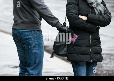 Midsection of young male robber stealing clutch from woman's jacket on street during winter Stock Photo