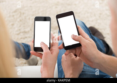 Cropped image of young couple using smart phones with blank screens at home Stock Photo