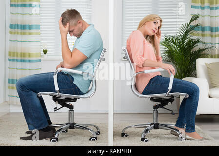 Full length side view of upset young couple sitting on chairs at home Stock Photo