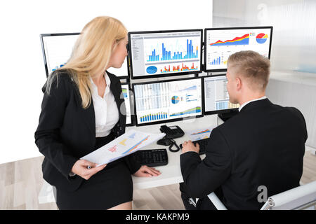Young financial workers analyzing graphs on desktop computers at desk in office Stock Photo