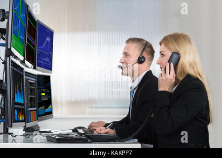 Young business people analyzing data displayed on computer screens in office Stock Photo