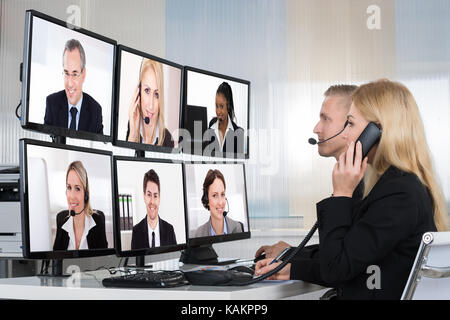 Business people having conference call with multiple computer screens at table in office Stock Photo