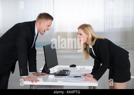 Young businessman and businesswoman shouting at each other at desk in office Stock Photo