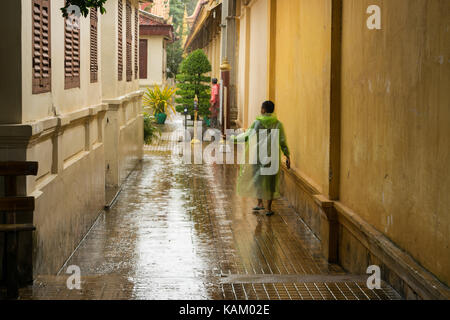 A teenager wearing a transparent green rain jacket, checking if the  the heavy monsoon rain stopped, after a heavy shower in Phnom Penh city, Cambodia Stock Photo